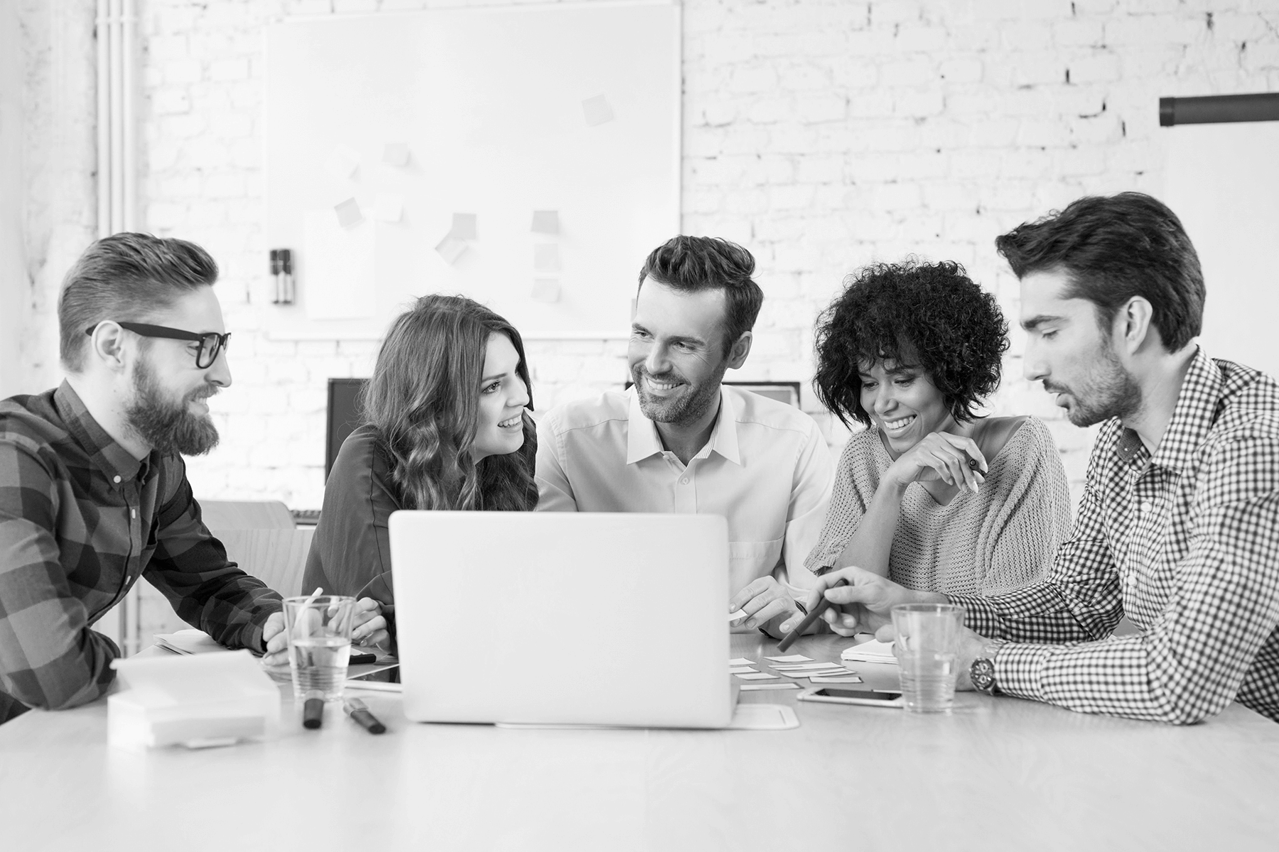 Faded background of five culturally diverse adults smiling and conversing around a laptop at their workplace