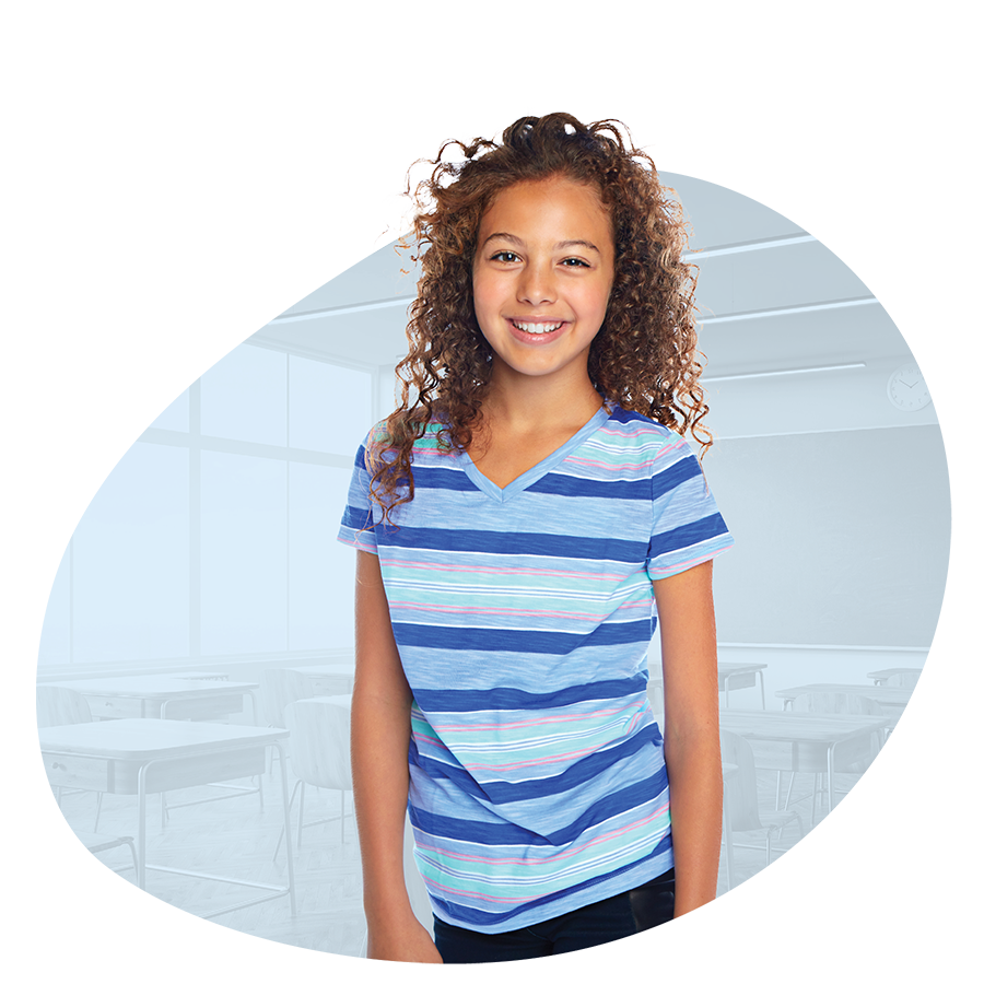 Cheerful seventh grade girl student with blue striped shirt in front of faded background of an empty classroom