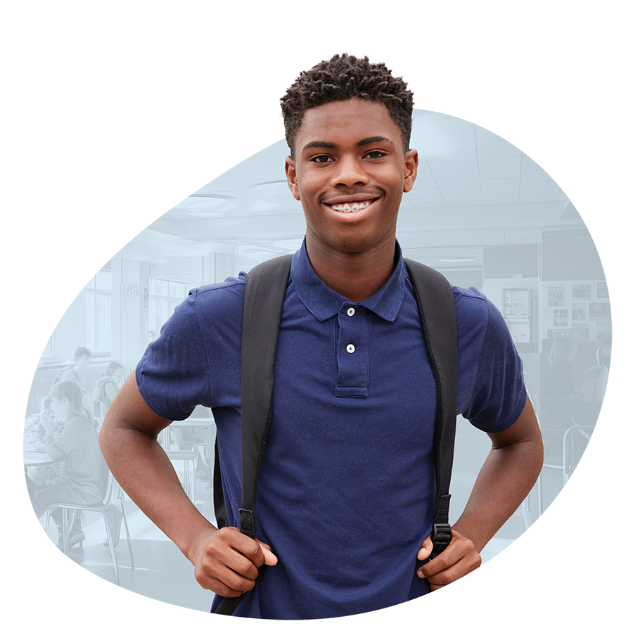 Teenage boy student with backpack and braces smiling in front of faded classroom background