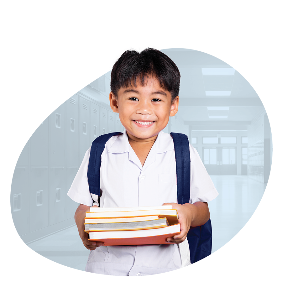 Smiling second grade boy student wearing backpack and holding a stack of books in front of a circular faded background of a school hallway